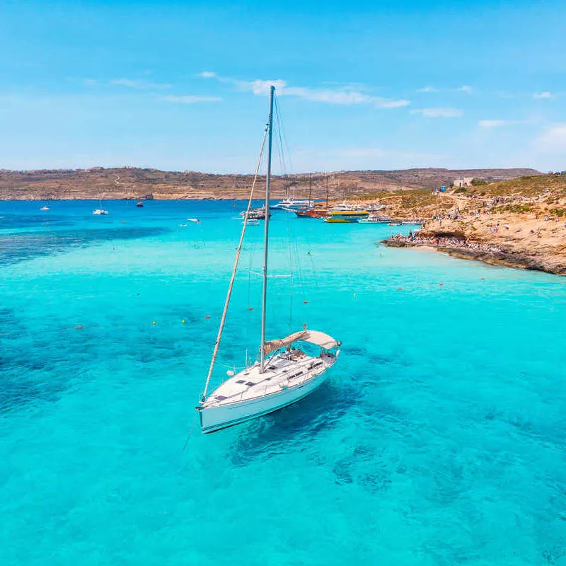 A Yacht Docked In The Middle Of The Blue Lagoon, On The Small Island Of Comino, Part Of Malta, A Southern European Country In The Mediterranean Sea