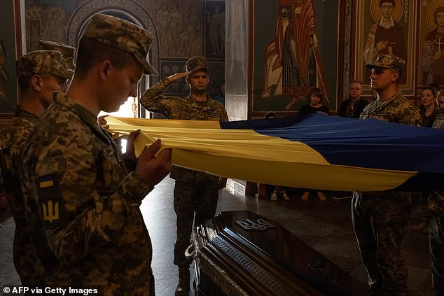 Ukrainian soldiers hold a national flag over the coffin of Ukrainian serviceman Ruslan Troianchuk, callsigned 