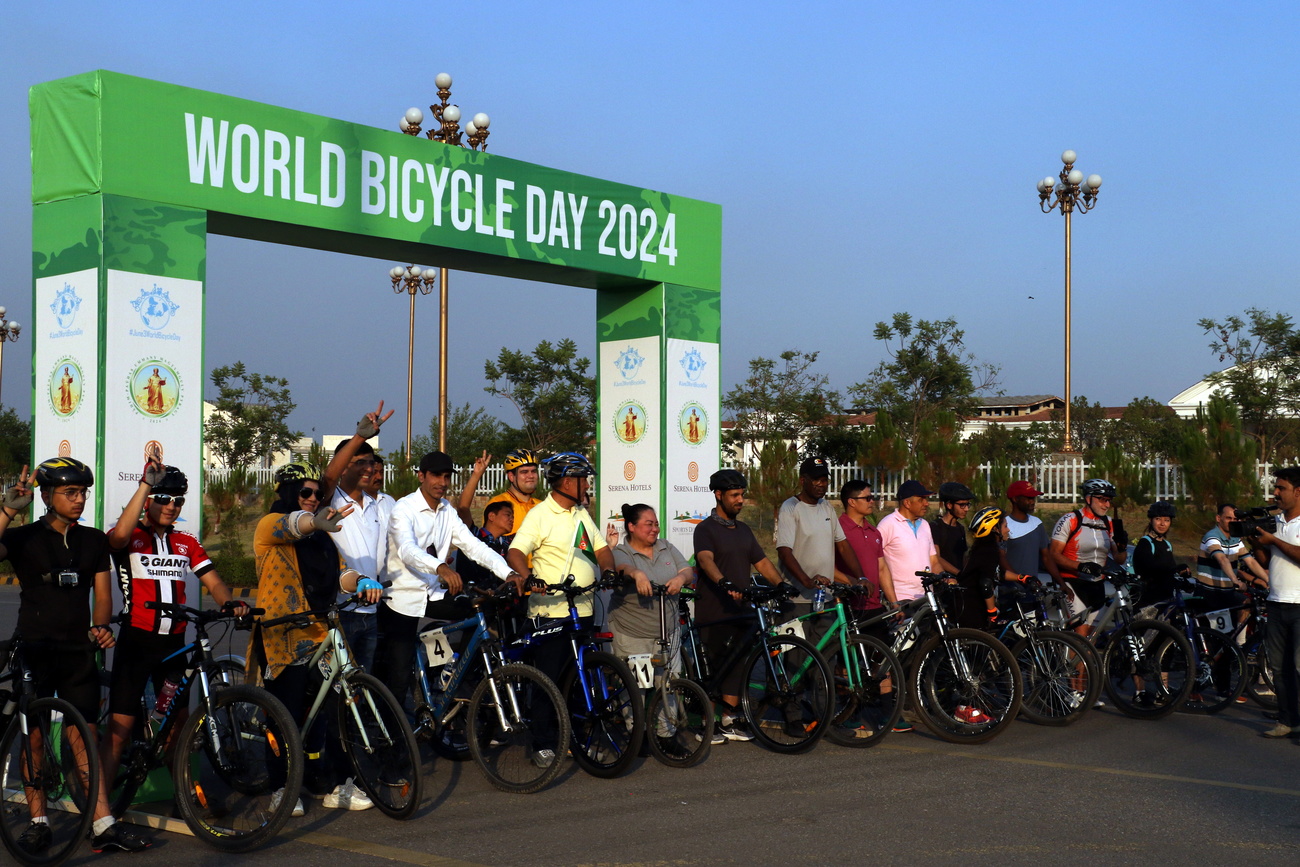 Many people on bicycles stand ready to ride in front of a banner that reads, 