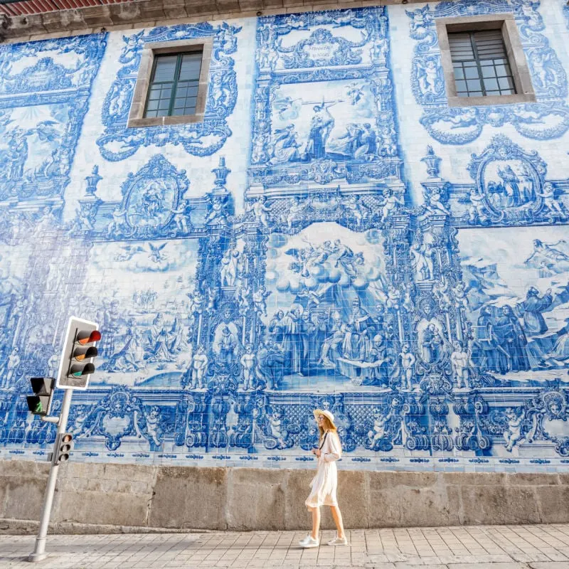 woman walks past blue ceramic tiles on building in porto portugal