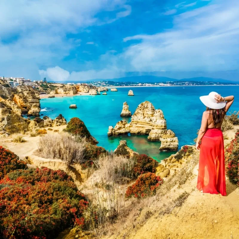 Woman looking at landscape with caves, grottoes and sea arches in Lagos, Algarve, Portugal