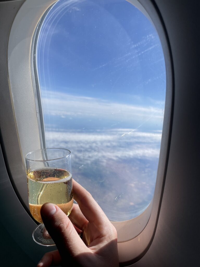 A passenger is holding up a glass of champagne in front of the aircraft window