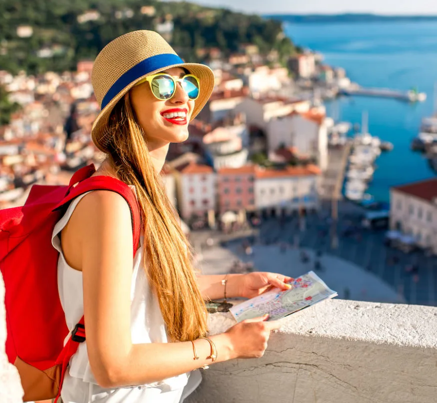 Young female traveler with red backpack and hat enjoying the view from George's tower on Piran old town. Traveling in Slovenia
