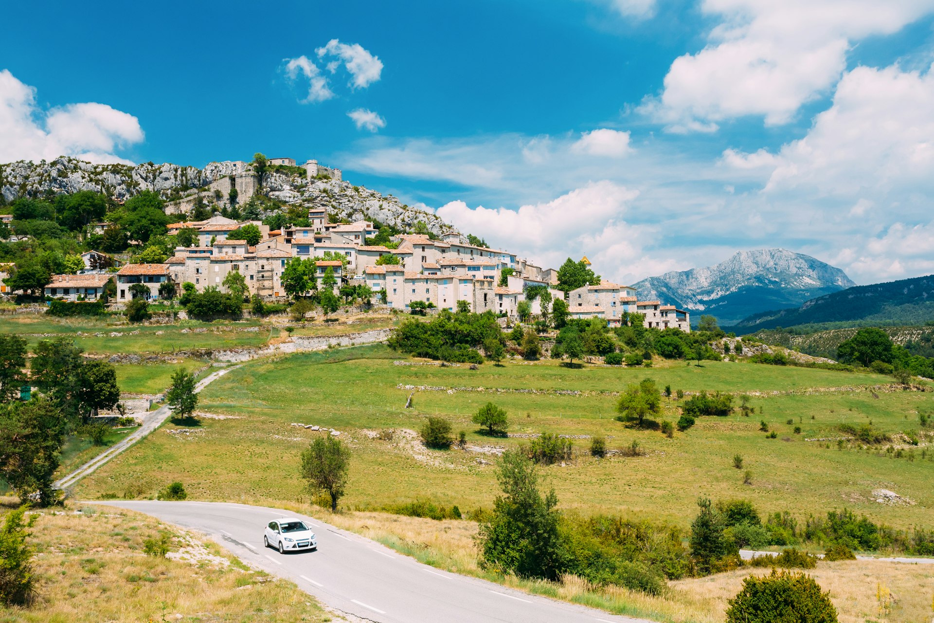 A Car drives along the road against a background of beautiful scenic view of a medieval village in France. 