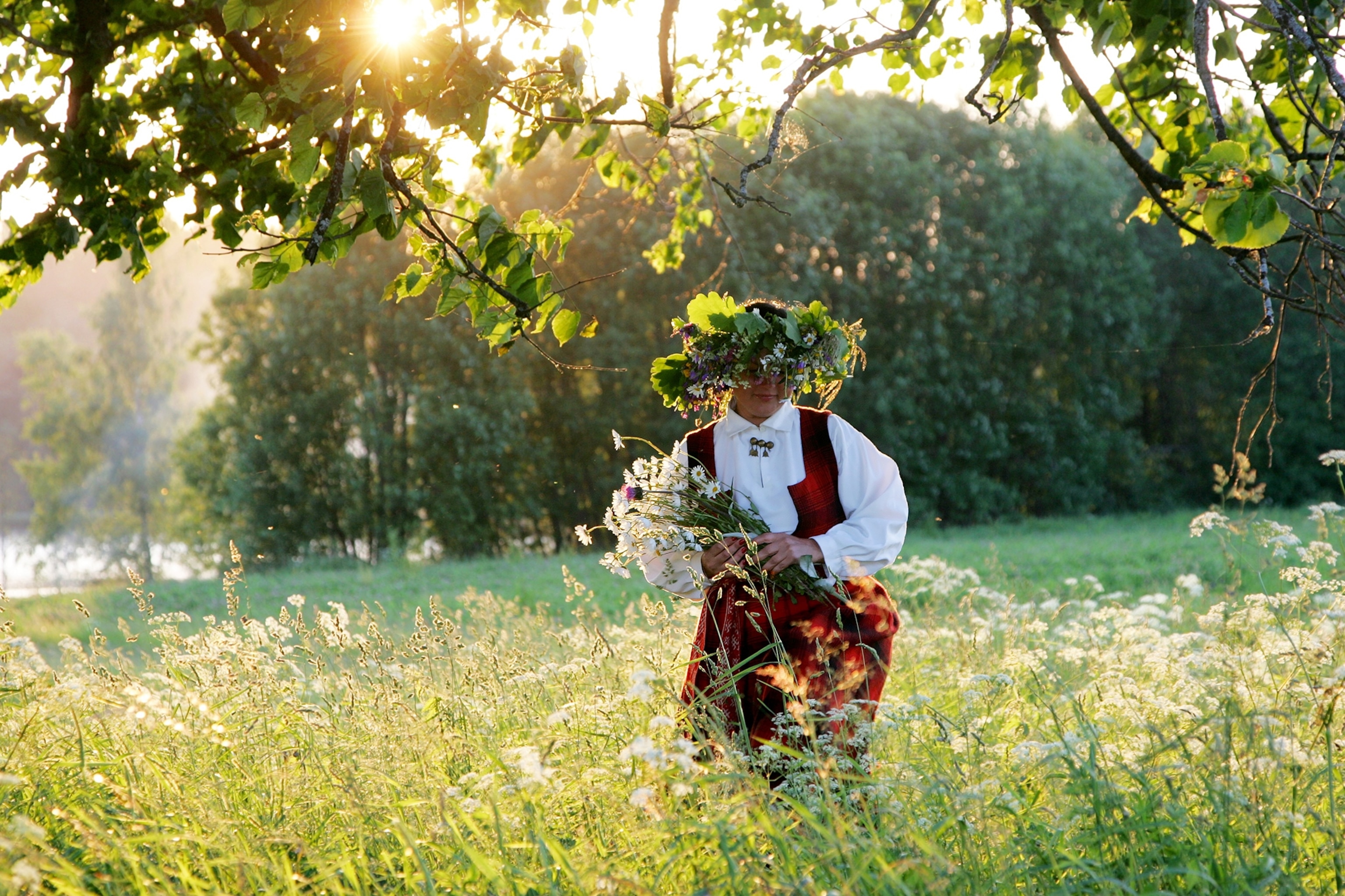 A woman in Latvia walking through a field on a sunny day whilst celebrating midsummer