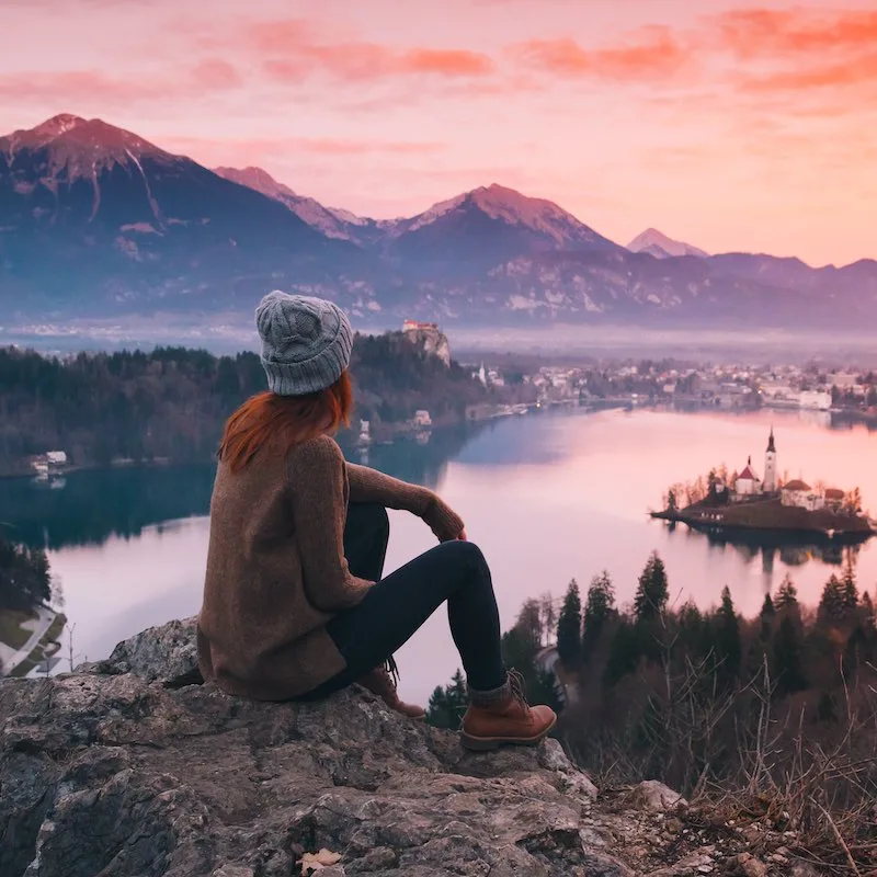 hiker at sunset resting on the cliffside overlooking a lake and church in the Tatras mountains in Slovenia