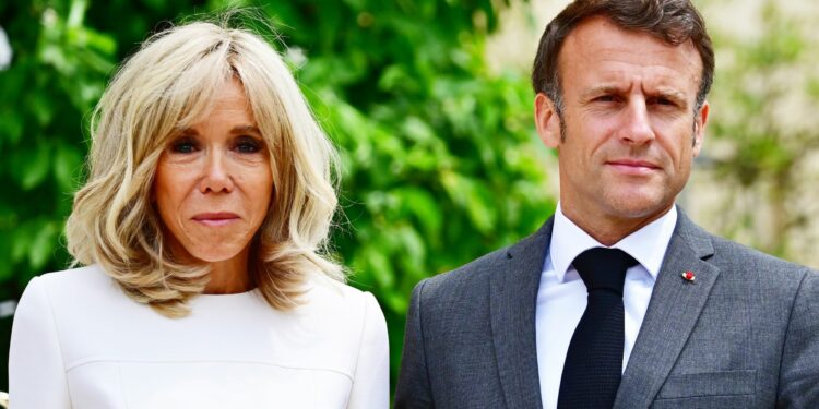 French president Emmanuel Macron wears a suit and tie as he stands beside his wife Brigitte, who is wearing white