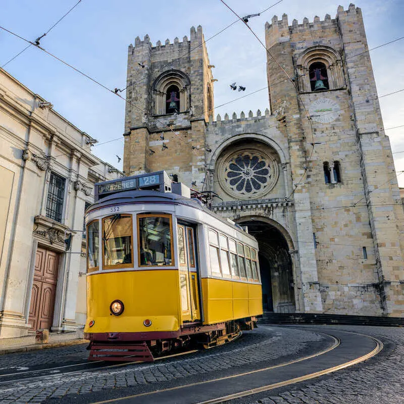 Yellow Tram Traveling Past Lisbon Cathedral In Lisbon, Portugal, Southern Europe