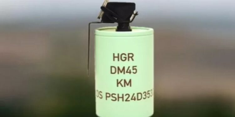 A Rheinmetall DM 45 hand grenade is displayed. The grenade has a cylindrical shape and is painted green, with