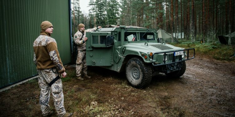 Soldiers from the Latvian National Armed Forces stand next to an armored Hummer vehicle