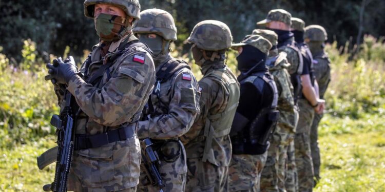 Armed Polish border guards stand next to a group of migrants on the border with Belarus