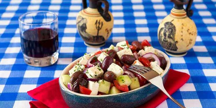 Greek drinks Greek salad with feta cheese tomatoes cucumber olives and onions with red wine and greek amphorae over a checkered tablecloth