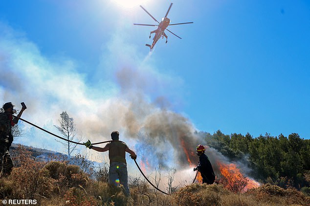 A firefighting helicopter flies over a firefighter and volunteers trying to extinguish a wildfire burning in Keratea, near Athens, Greece, June 30