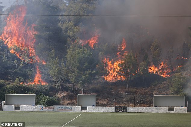 Flames rise next to a football stadium as a wildfire burns in Stamata, near Athens, Greece, June 30