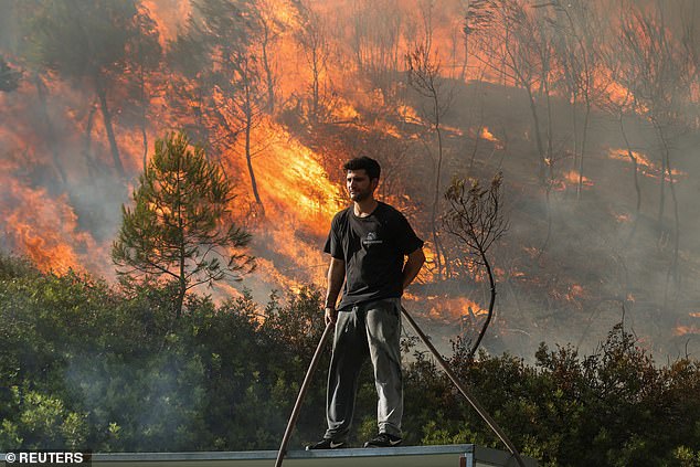 A volunteer stands on a roof as flames rise from a wildfire burning in Stamata, near Athens, Greece, June 30