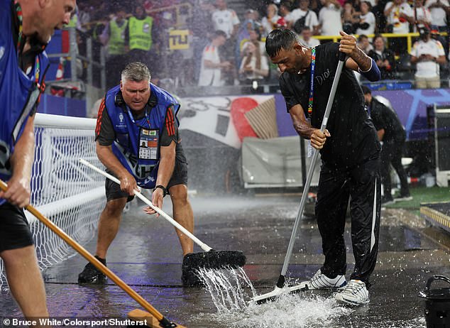Groundsman work to clear water after play is suspended due to adverse weather conditions at the euros clash between Germany and Denmark on June 29