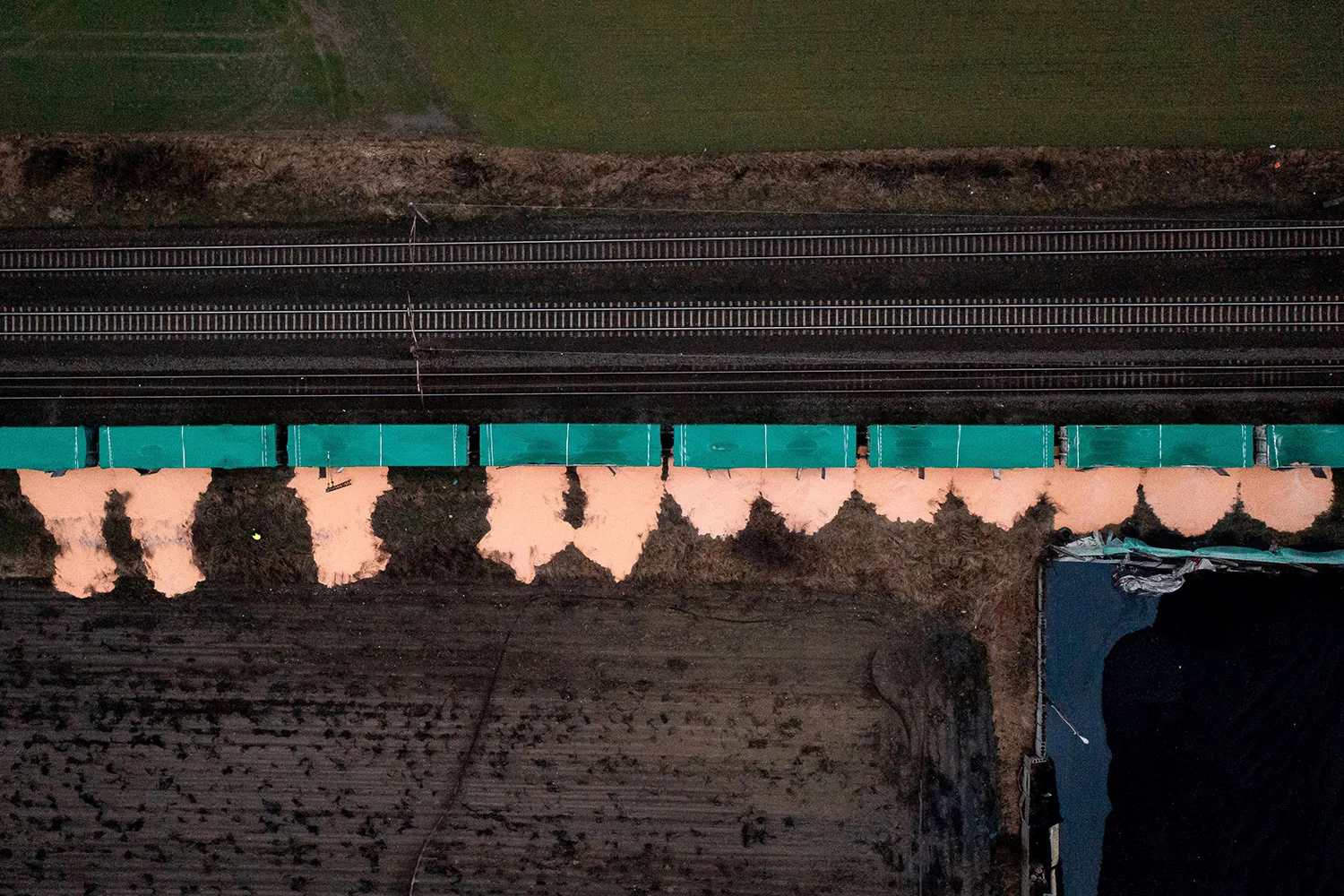An aerial view shows piles of corn lying next to eight teal train cars on railroad tracks in the village of Kotomierz, Poland.
