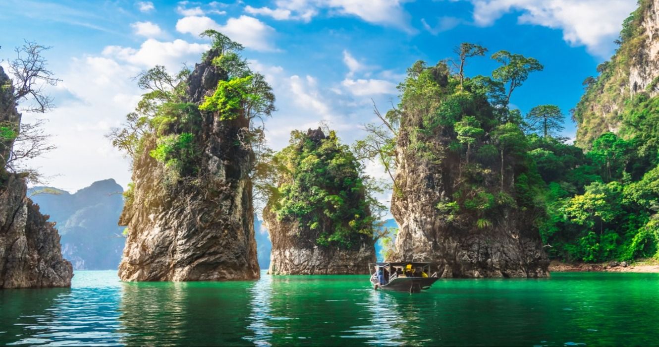 A boat on the blue water approaching dramatic rock formations in Khao Sok National Park, Thailand