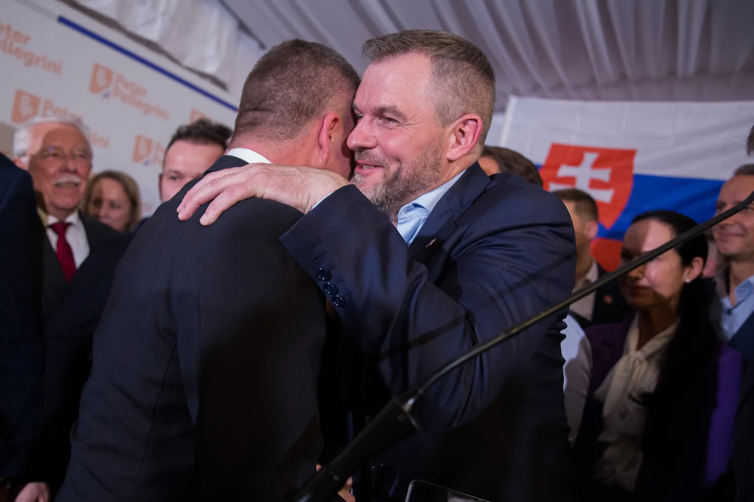 Two men in suits hug in a crowd.