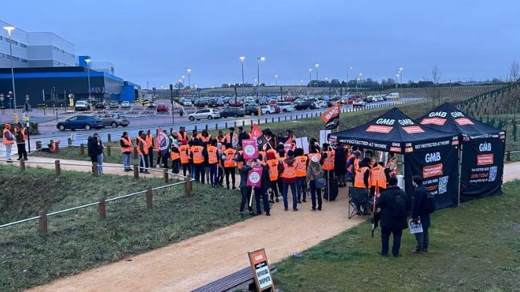 Workers in high-visibility jackets at kiosks with GMB logos outside Amazon