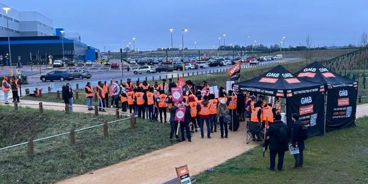 Workers in high-visibility jackets at kiosks with GMB logos outside Amazon