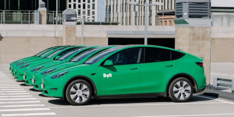 Multiple green Tesla vehicles with the Bolt logo on the side, in a car park.