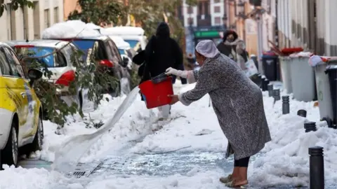 Reuters A woman throws water on a snow-covered street, following heavy snowfall, in Madrid, Spain January 11, 2021