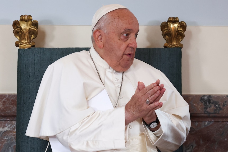 Pope Francis holds his hands together in a gesture to an off-camera speaker.