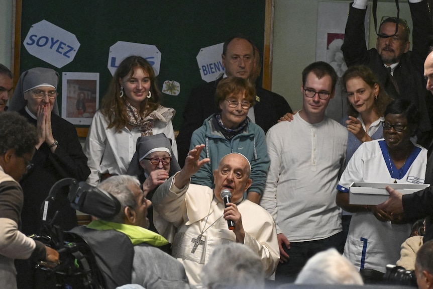 Pope Francis raises a hand as he speaks into a microphone surrounded by Belgians.