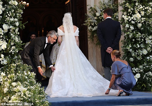 Princess Theodora of Greece stands at the foot of the cathedral as her dress is delicately repositioned