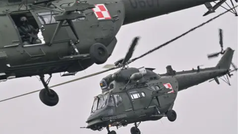 Omar Marques/Anadolu  Polish helicopters fly over soldiers in their tanks while crossing the Vistula River during the DRAGON-24 NATO military defense drills on March 04, 2024