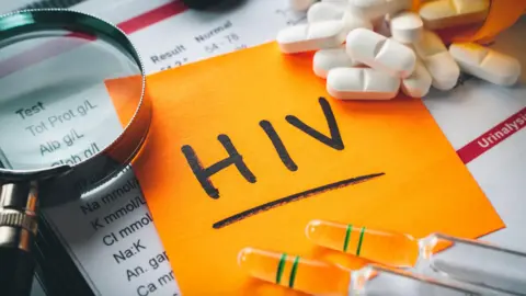 Getty Images Orange paper with the word 'HIV' on it, alongside pills, a microscope and vials of liquid