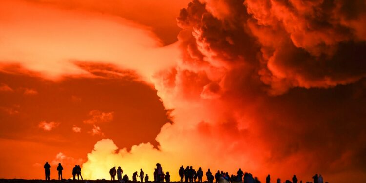 Silhuoettes of people standing infront of the bright orange sky that has volcanic gas clouds in the air.