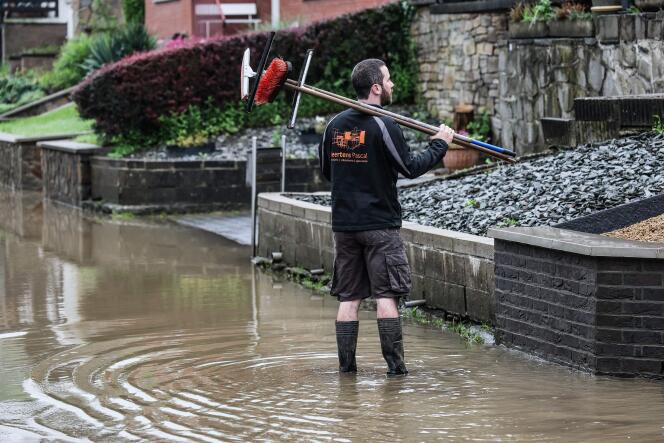 A local resident holds squeegees and sweepers in a flooded street the day after an episode of heavy rain in Trooz, Belgium, on May 18, 2024.