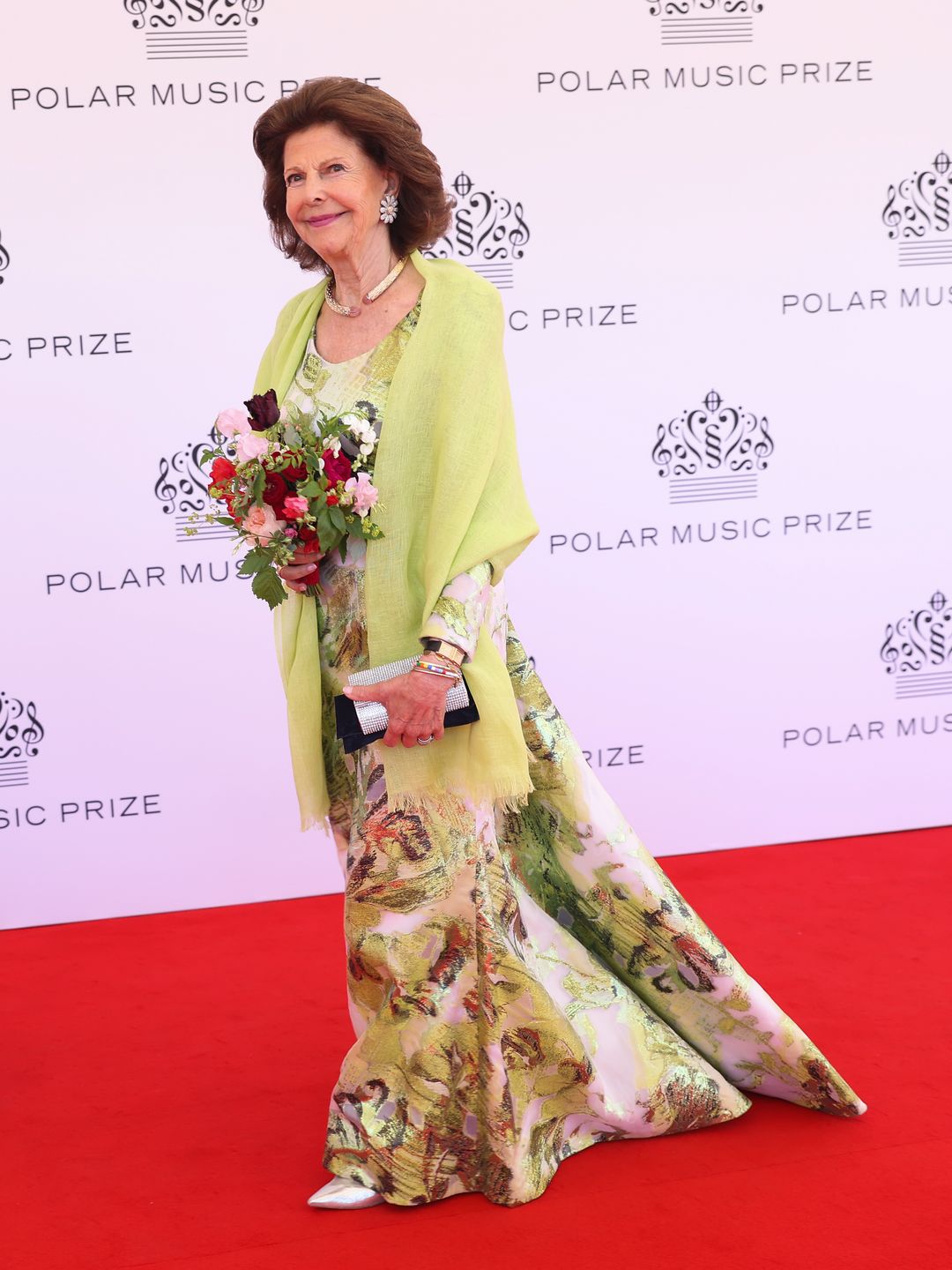 Full-body image of Queen Silvia in a yellow and floral dress