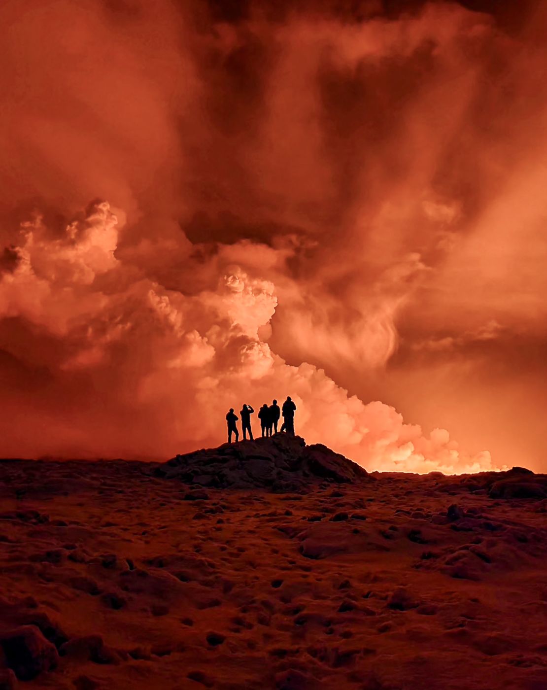 Local resident watch smoke billow as the lava colour the night sky orange from an volcanic eruption on the Reykjanes peninsula 3 km north of Grindavik, western Iceland on December 19, 2023. A volcanic eruption began on Monday night in Iceland, south of the capital Reykjavik, following an earthquake swarm, Iceland's Meteorological Office reported. (Photo by Kristin Elisabet Gunnarsdottir / AFP) (Photo by KRISTIN ELISABET GUNNARSDOTTIR/AFP via Getty Images)