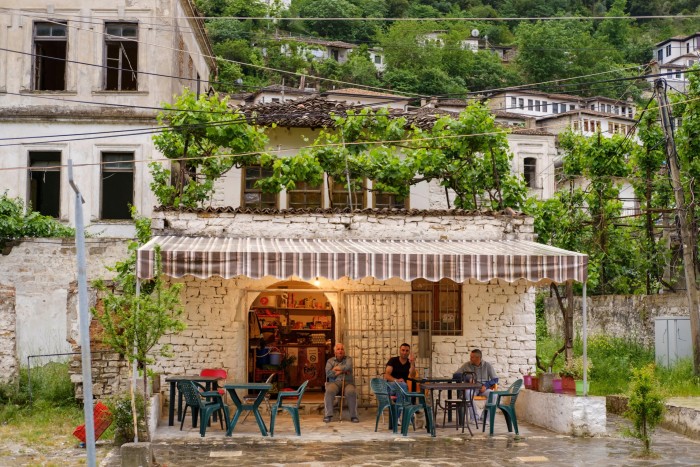 Three men sit under an awning on the terrace of a small restaurant