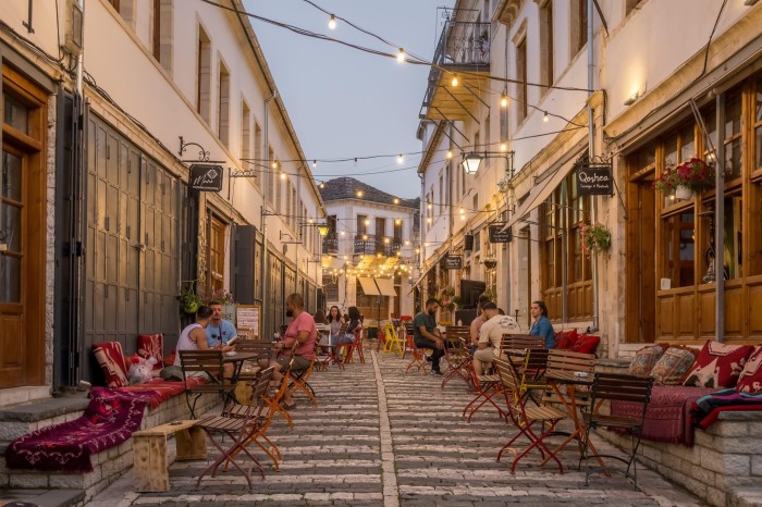 A cobbled path between buildings, with open air cafes and fairy lights