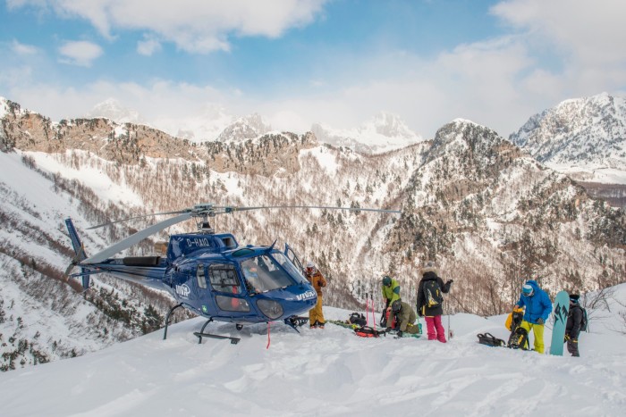 Skiers wait next to a helicopter on a snow covered mountain