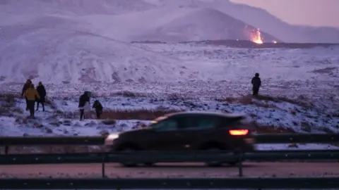 EPA Onlookers gather to watch the lava flow after a volcanic eruption near the town of Grindavik, Reykjanes peninsula, Iceland, 19 December 2023. The start of a volcanic eruption was announced by Iceland's Meteorological Office on 18 December night after weeks of intense earthquake activity in the area.