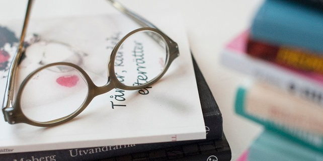 A pair of eyeglasses rests on top of a pile of books.