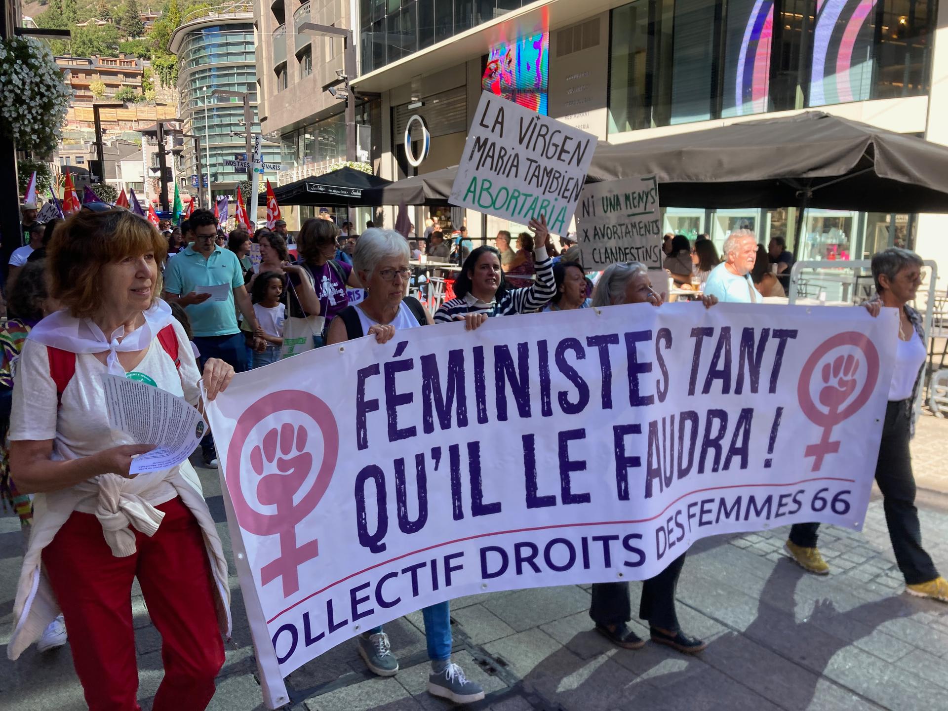 Mostly female protestors walking in a small street with a large white banner