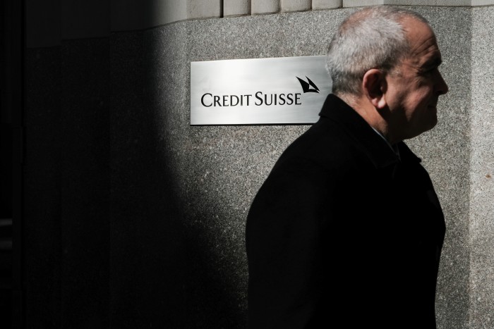 A grey-haired man walks past a sign of Credit Suisse attached on the exterior of a building