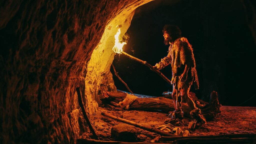 A recreation of an ancient human wearing furs and holding a torch walking into a cave