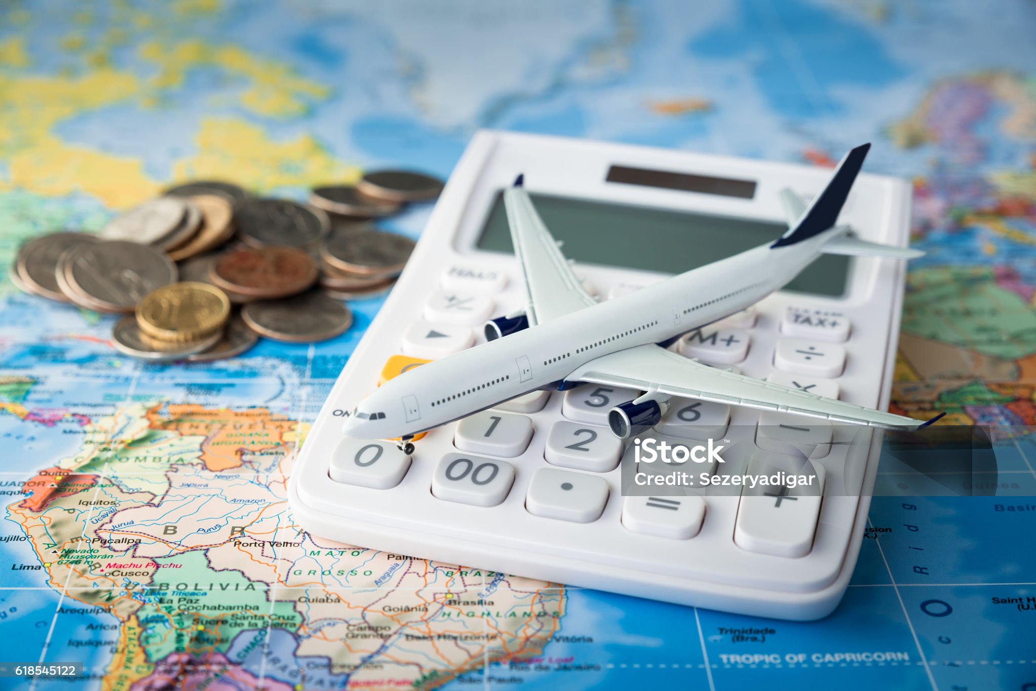 Toy plane on a calculator with coins on a map, symbolizing travel costs and budgeting.