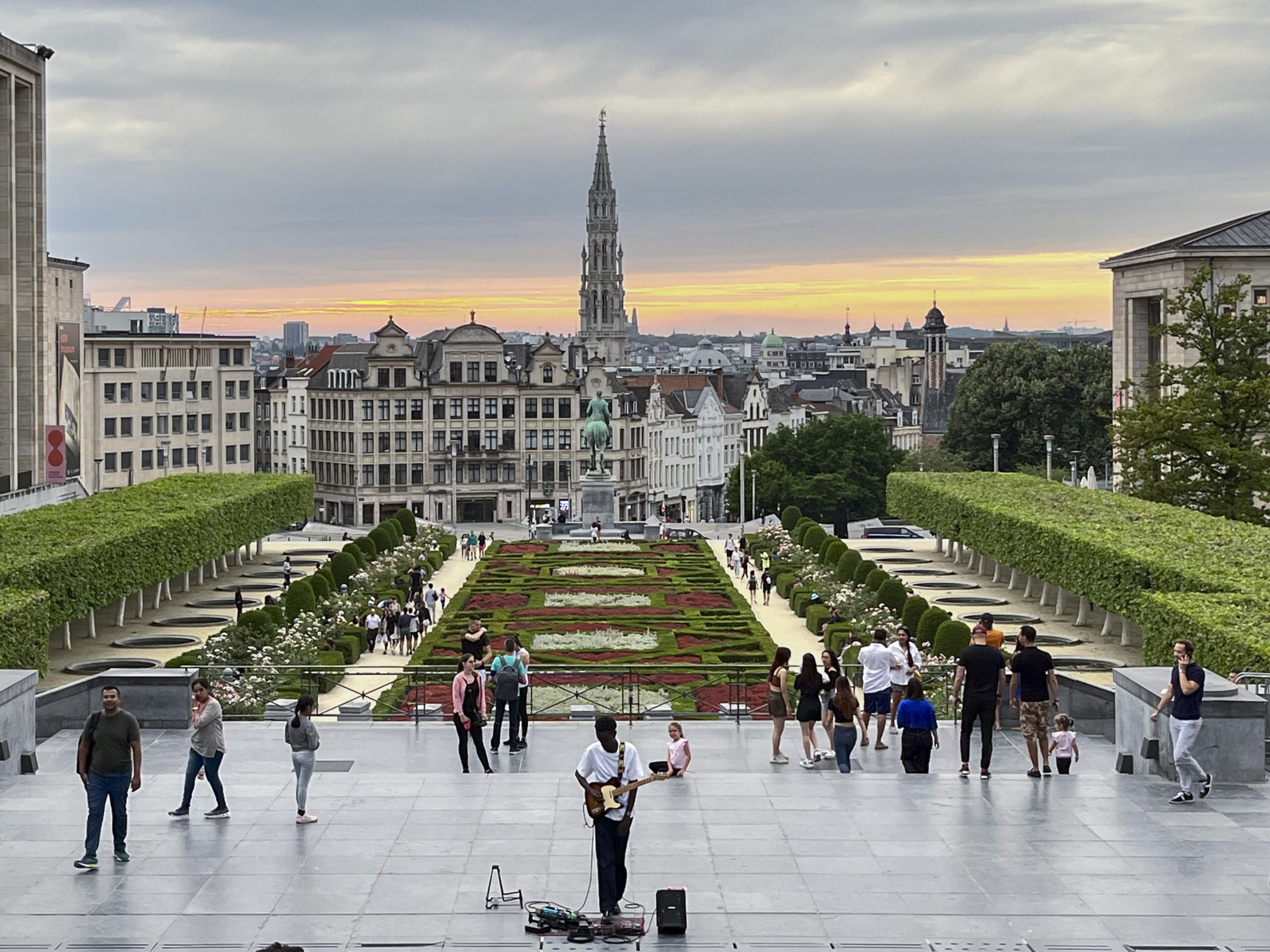 A busker sings to entertain people enjoying the views and the sunset at Mont des Arts (Kunstberg in Dutch)—an urban complex and historic site in central Brussels—with the spire of the town hall rising in the distance. Photo by Mahvish S. Khan