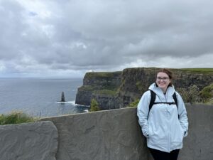 Sydney Dooley-Smith '26 wears a jacket and backpack while posing in front of the Cliffs of Moher.