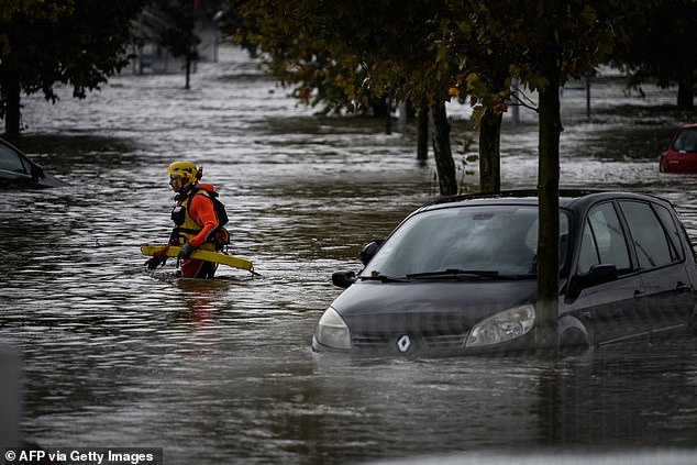 A firefighter wades through floodwaters past a partially submerged car parked in a shopping area today in Givors