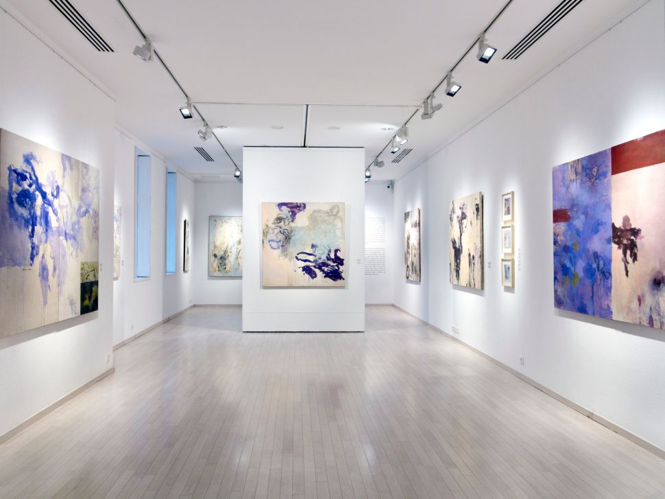 A white-walled art gallery with tall ceilings - there are large paintings on the walls