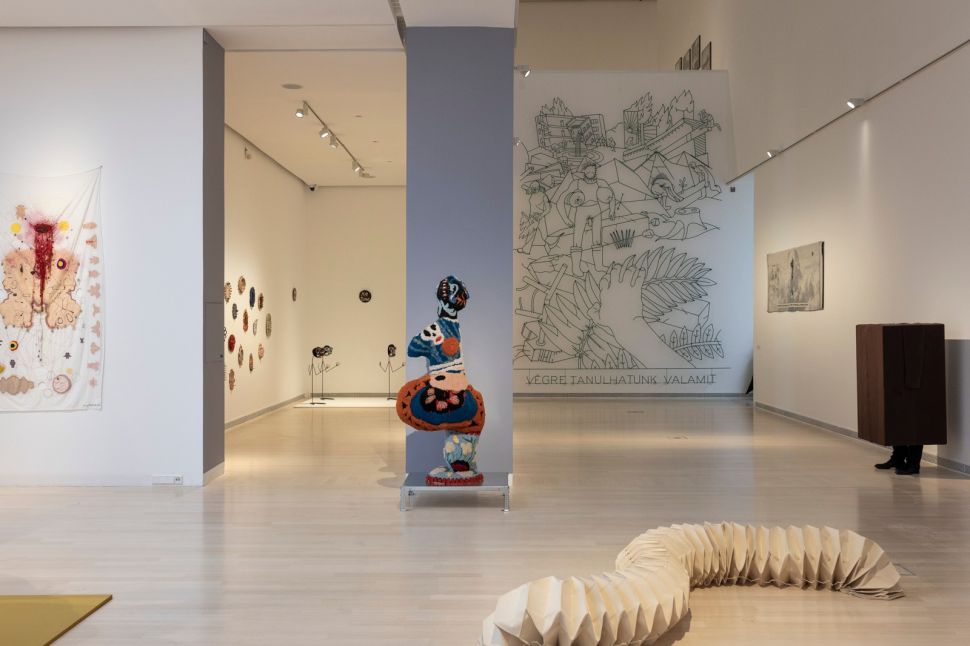 A dimly lit art gallery with paintings on the walls and floor sculptures